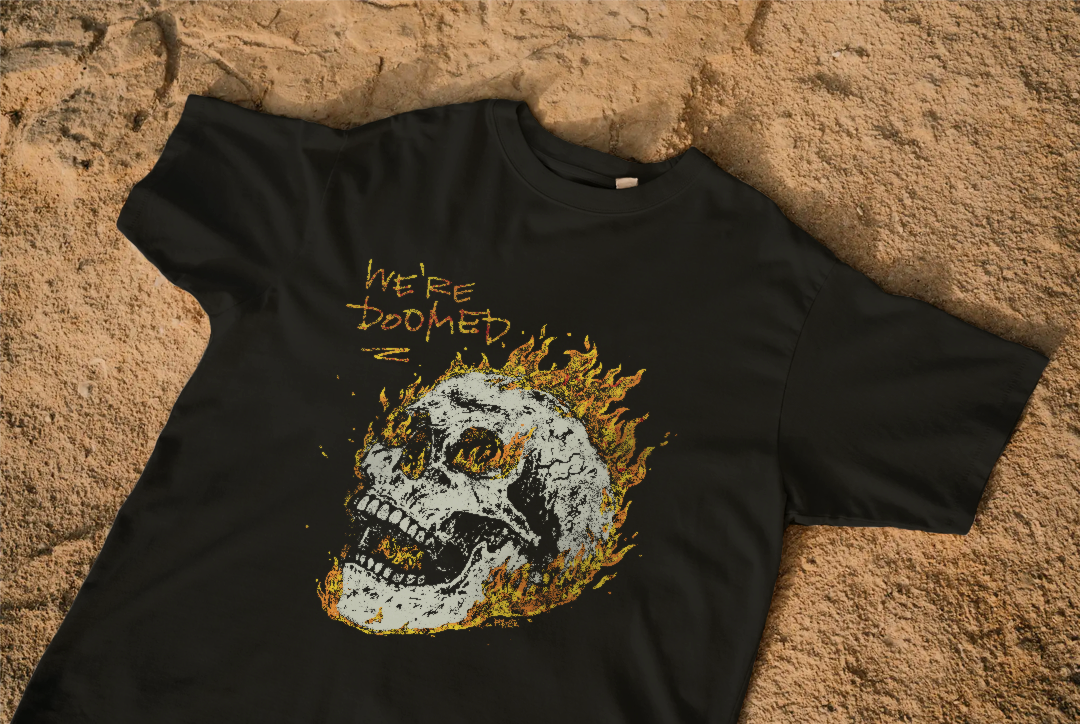 black T-shirt laying on the ground, with a graphic of a burning skull on it, saying "we're doomed"