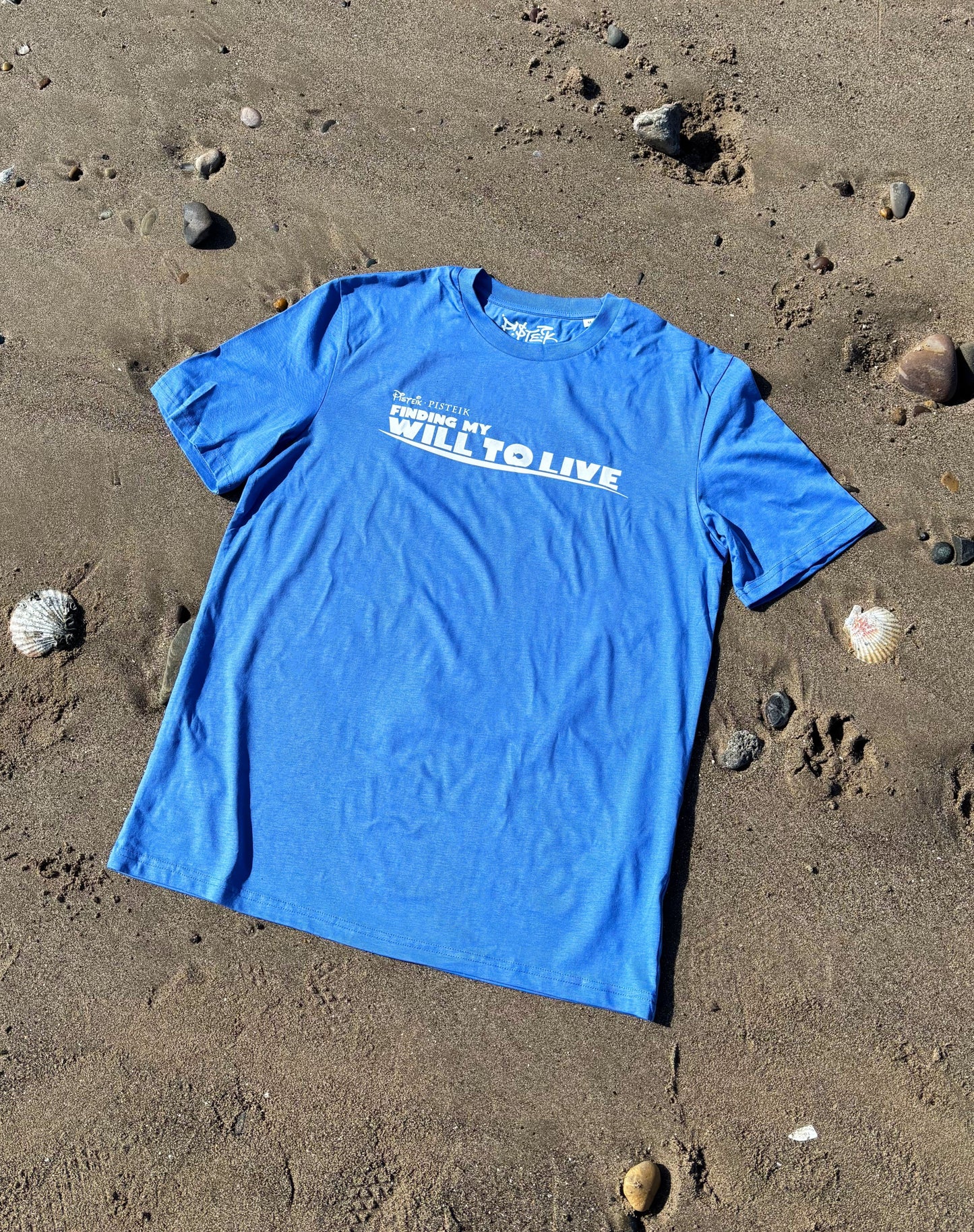 blue t-shirt on the beach surrounded by seashells; graphic print saying "finding my will to live"